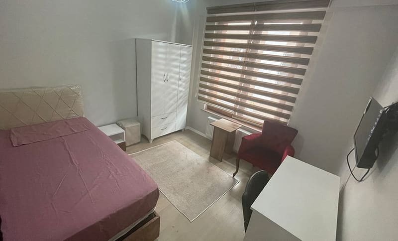 Yatak, dolap, koltuk, çalışma masası ve duvar ekranı bulunan oda