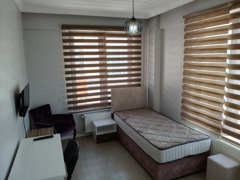 Pencere önünde yatak, komodin, çalışma masası ve koltuk bulunan oda