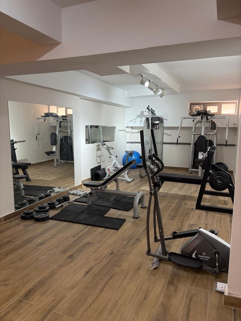 Aynalı spor salonunda ağırlık istasyonları, ayarlanabilir sehpa, bench press, kondisyon bisikleti ve eliptik bisiklet